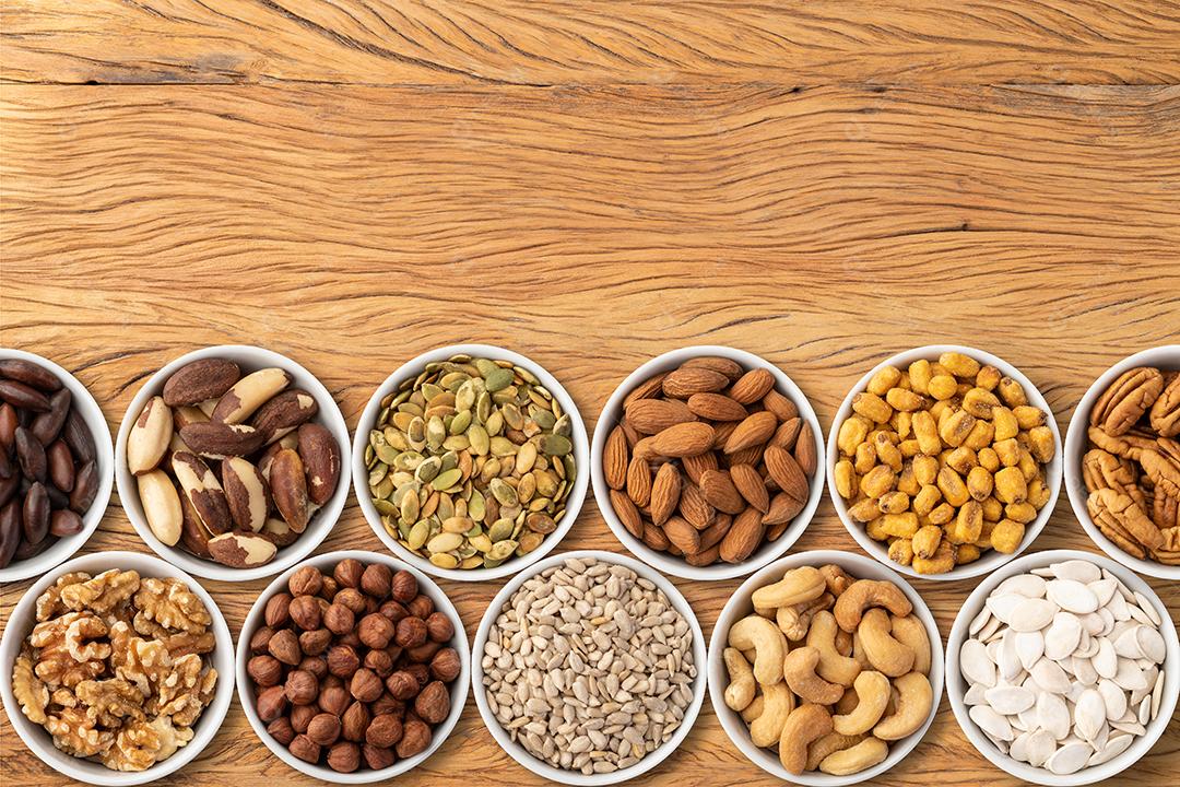 Nozes e sementes variadas em tigelas sobre mesa de madeira