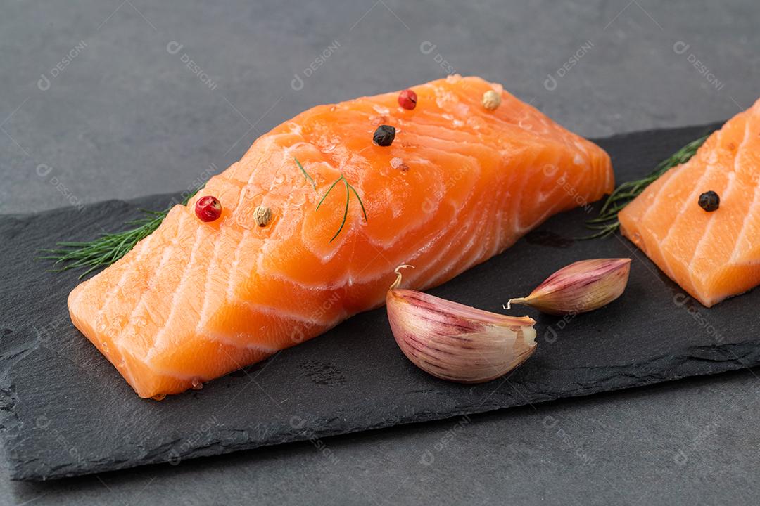 Fatias de salmão cru com temperos sobre placa de pedra.