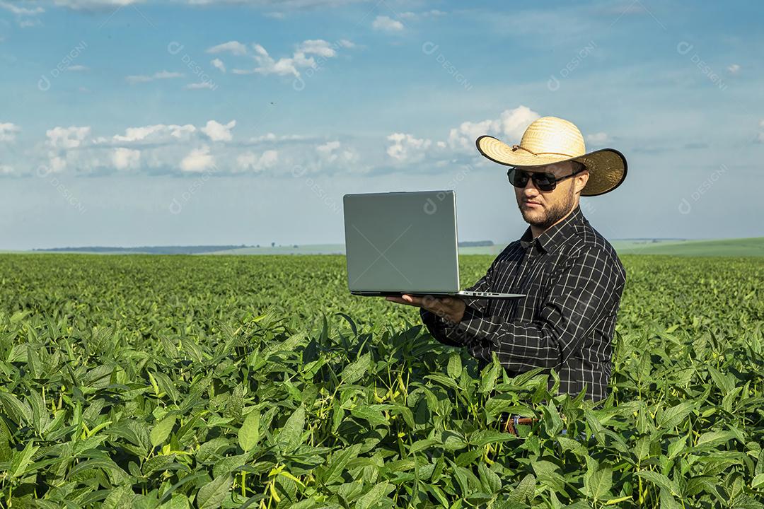 Jovem agricultor de chapéu segurando soja no campo de soja Imagem JPG