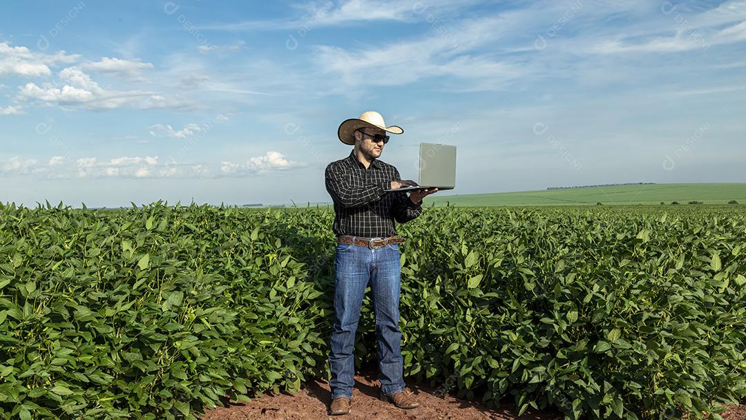 Jovem agricultor de chapéu segurando soja no campo de soja Imagem JPG
