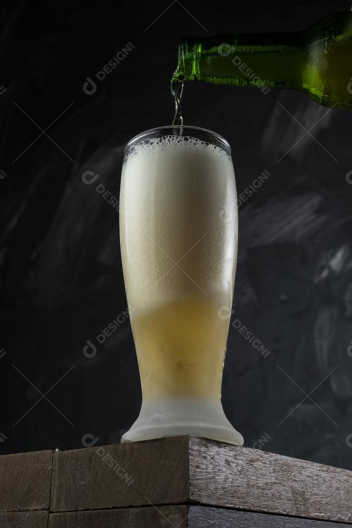 Cerveja derramando em copo em um bar. Mesa de madeira e fundo cinza