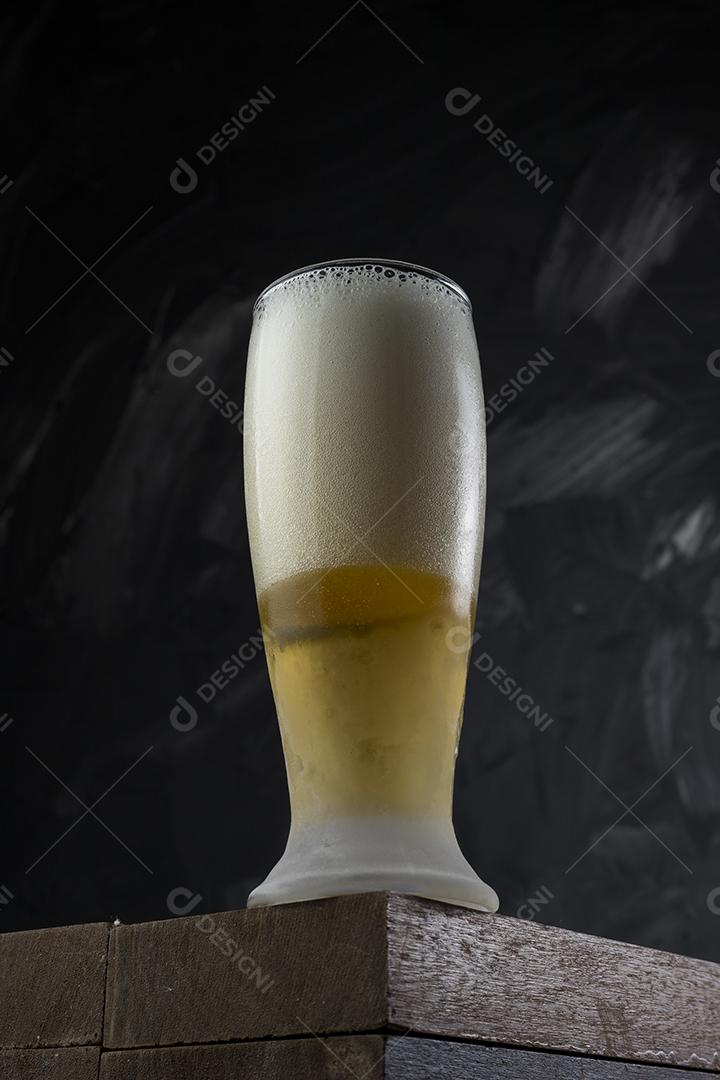Copo cheio de cerveja. Cerveja congelante em uma mesa de madeira e cinza