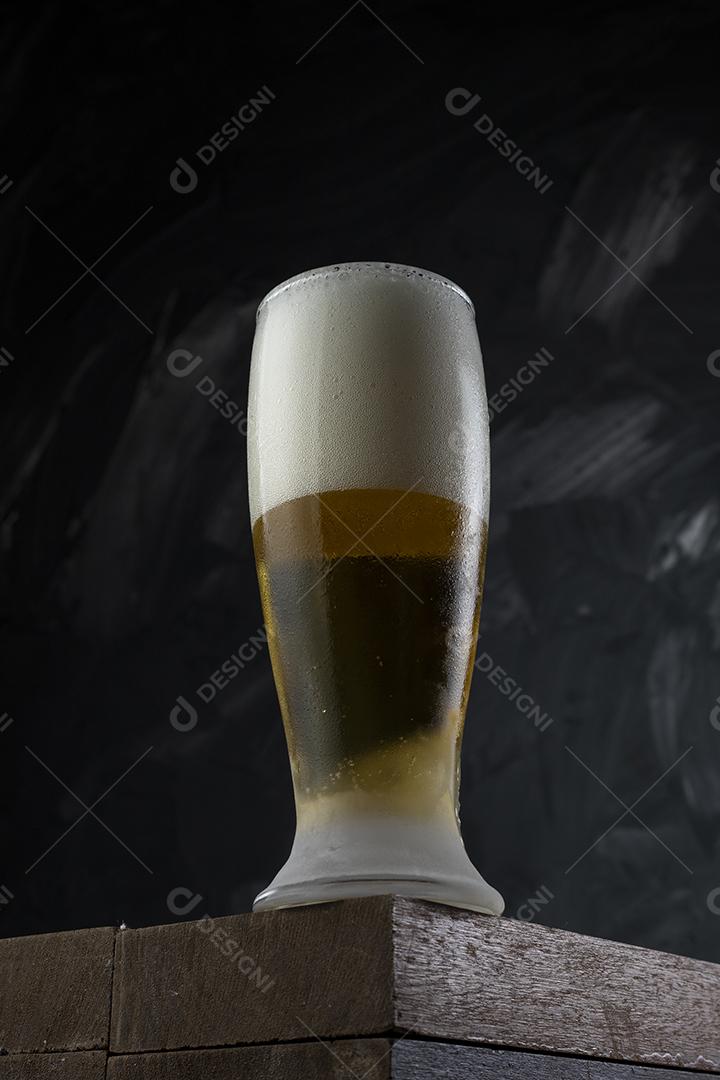 Copo cheio de cerveja. Cerveja congelante em uma mesa de madeira e cinza