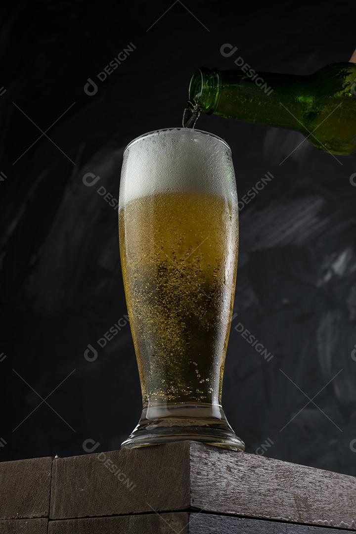 Cerveja derramando em copo em um bar. Mesa de madeira e fundo cinza