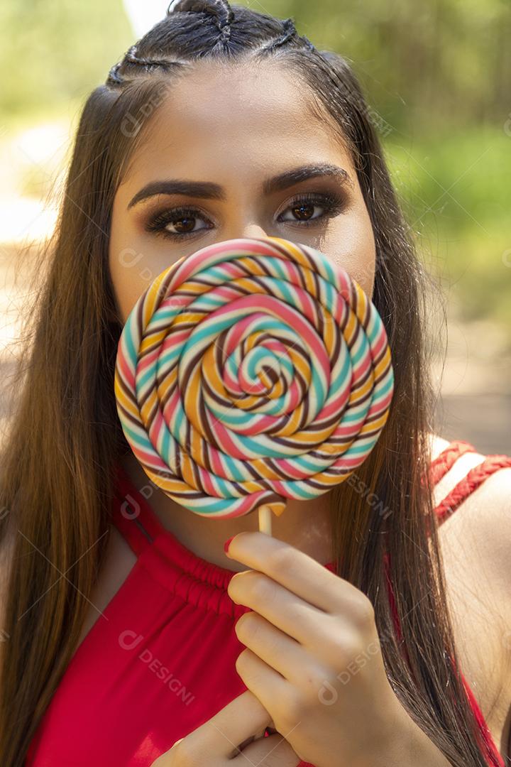 Linda menina morena segurando pirulito colorido na floresta
