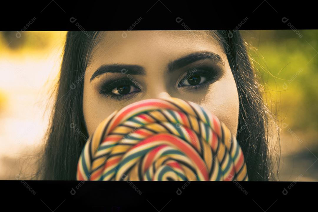 Linda menina morena segurando pirulito colorido na floresta