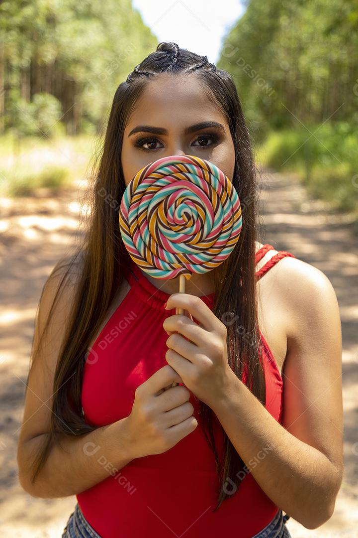Linda menina morena segurando pirulito colorido na floresta