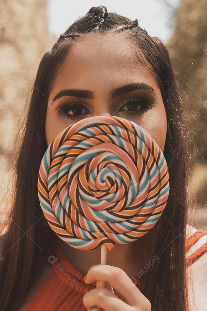 Linda menina morena segurando pirulito colorido na floresta