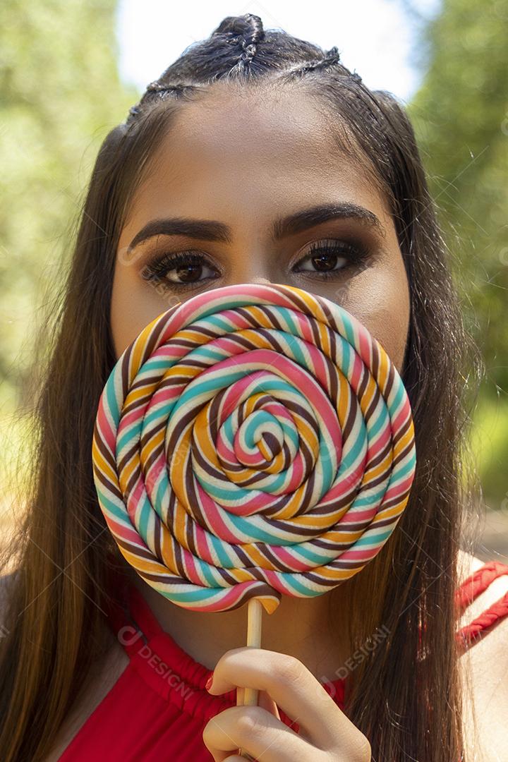 Linda menina morena segurando pirulito colorido na floresta