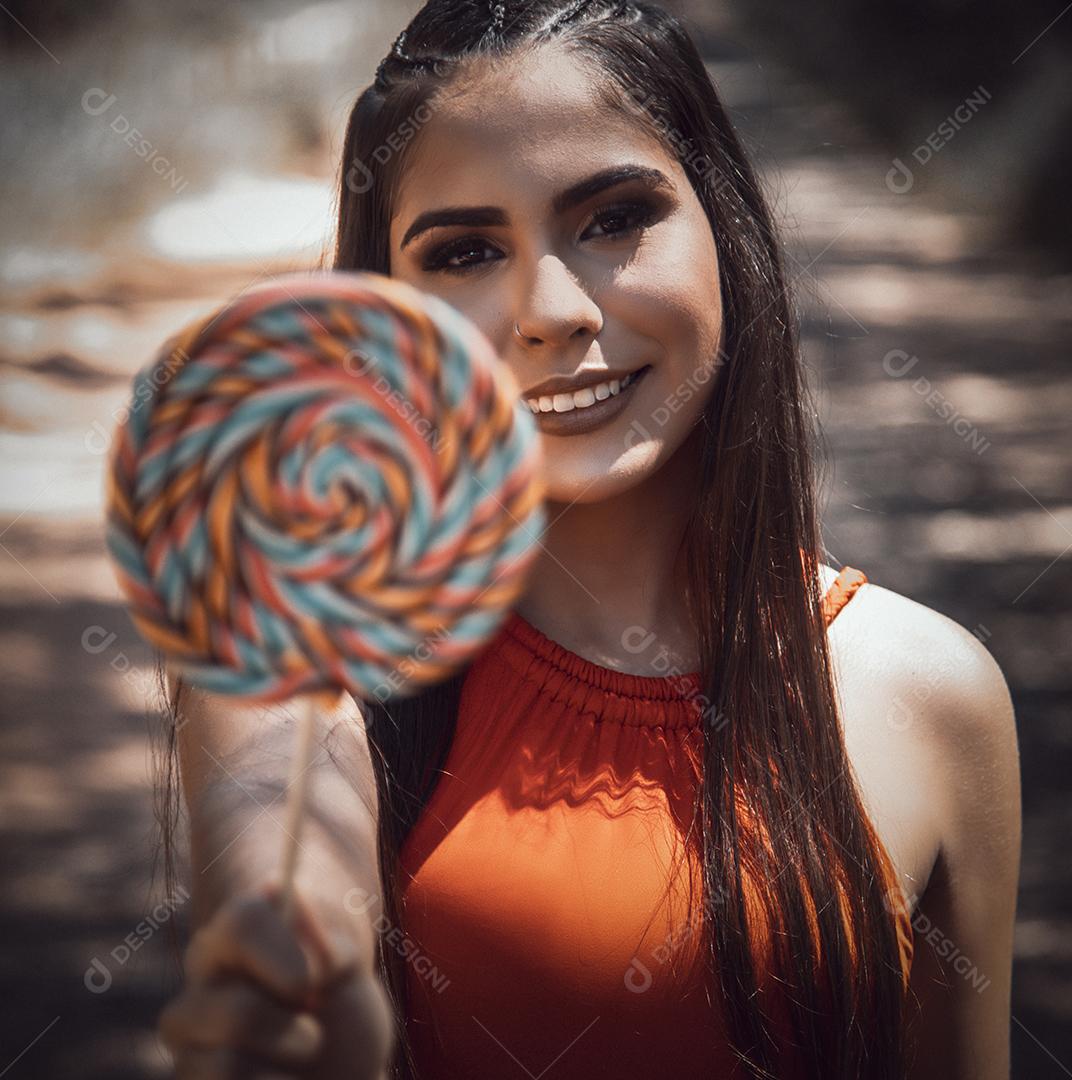 Linda menina morena segurando pirulito colorido na floresta