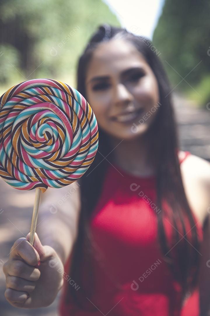 Linda menina morena segurando pirulito colorido na floresta