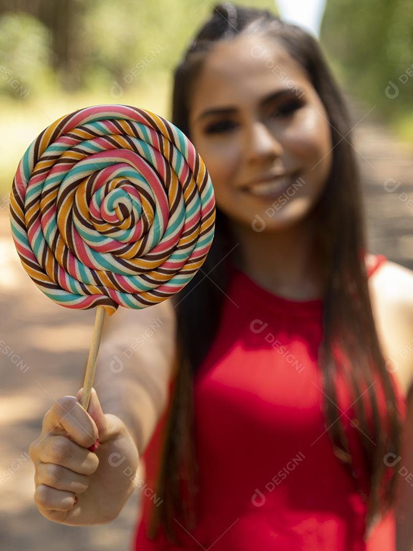 Linda menina morena segurando pirulito colorido na floresta
