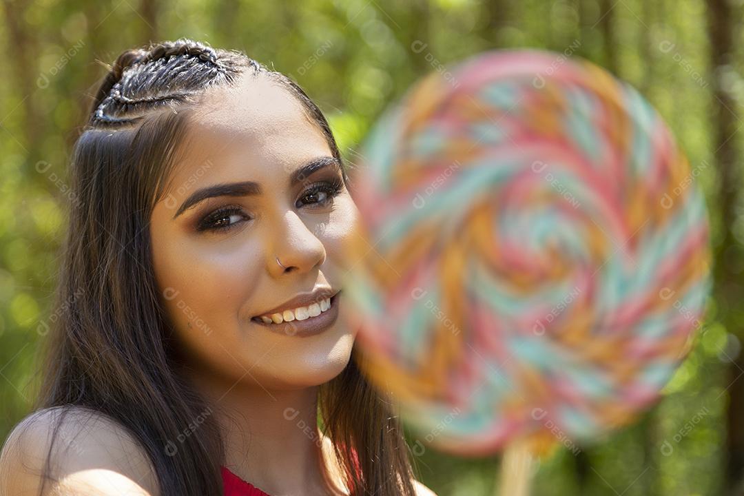 Linda menina morena segurando pirulito colorido na floresta