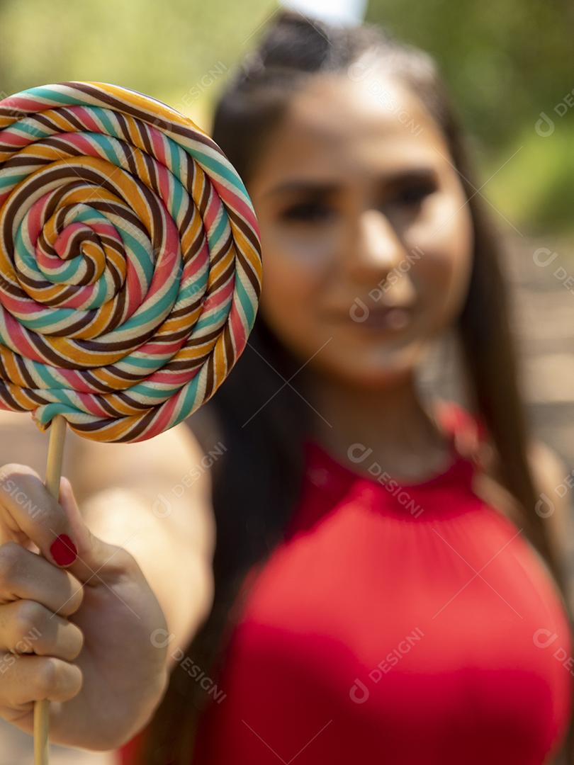 Linda menina morena segurando pirulito colorido na floresta