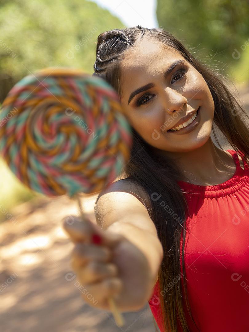 Linda menina morena segurando pirulito colorido na floresta