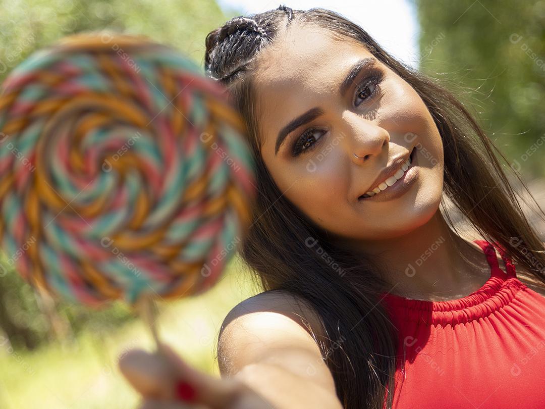 Linda menina morena segurando pirulito colorido na floresta