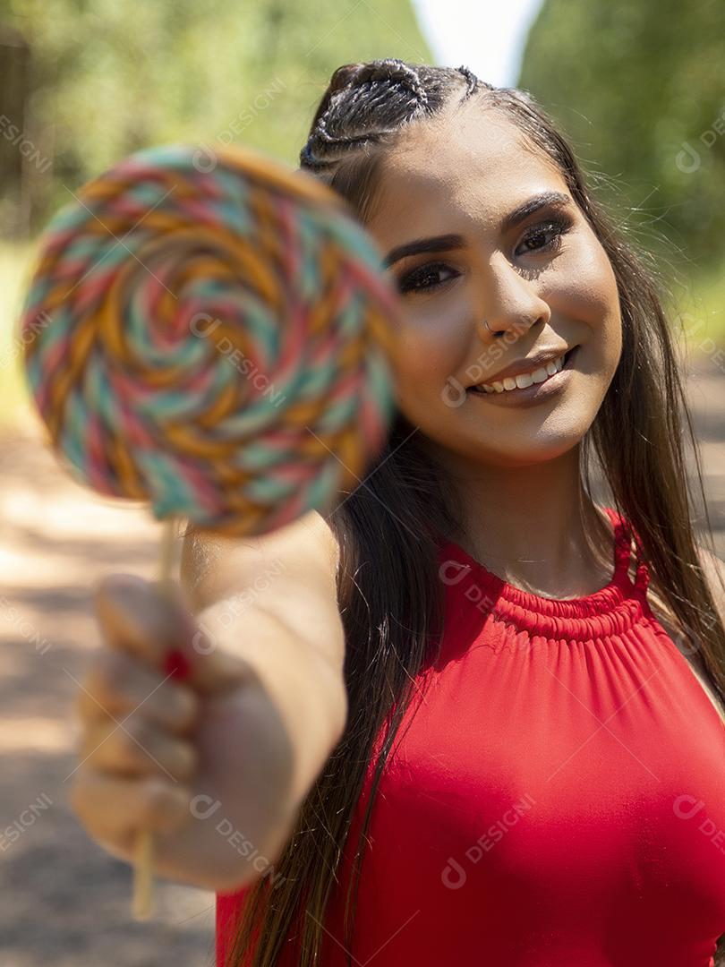 Linda menina morena segurando pirulito colorido na floresta