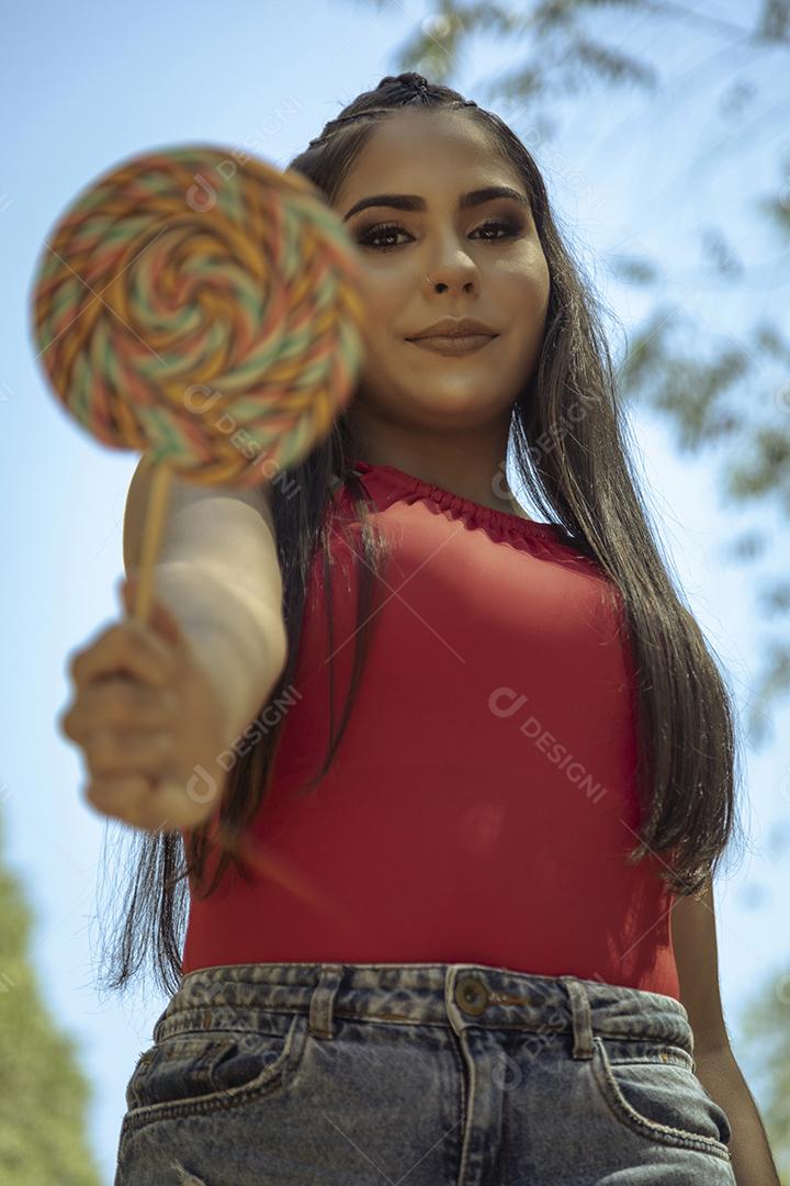 Linda menina morena segurando pirulito colorido na floresta