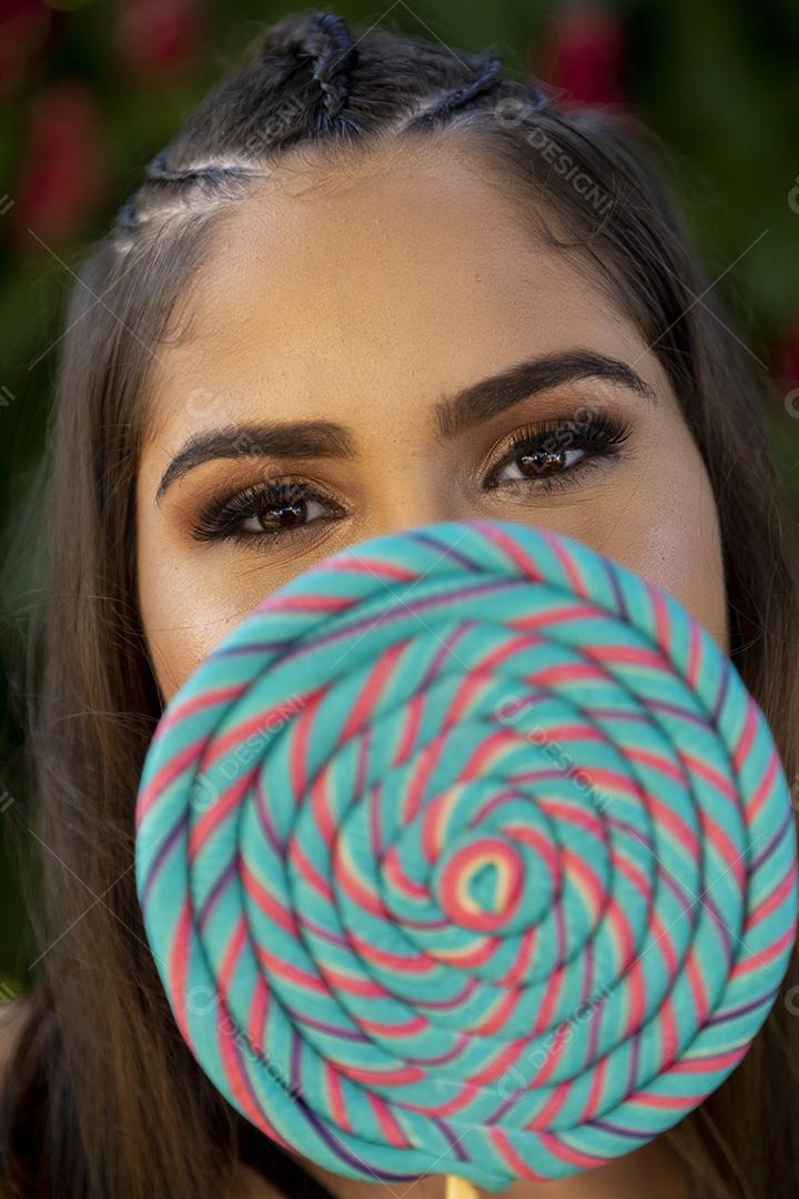 Linda menina morena segurando pirulito colorido na floresta