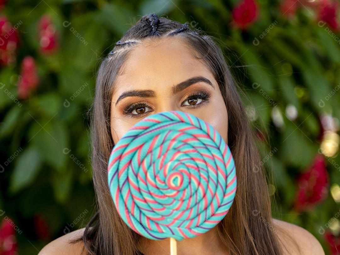 Linda menina morena segurando pirulito colorido na floresta