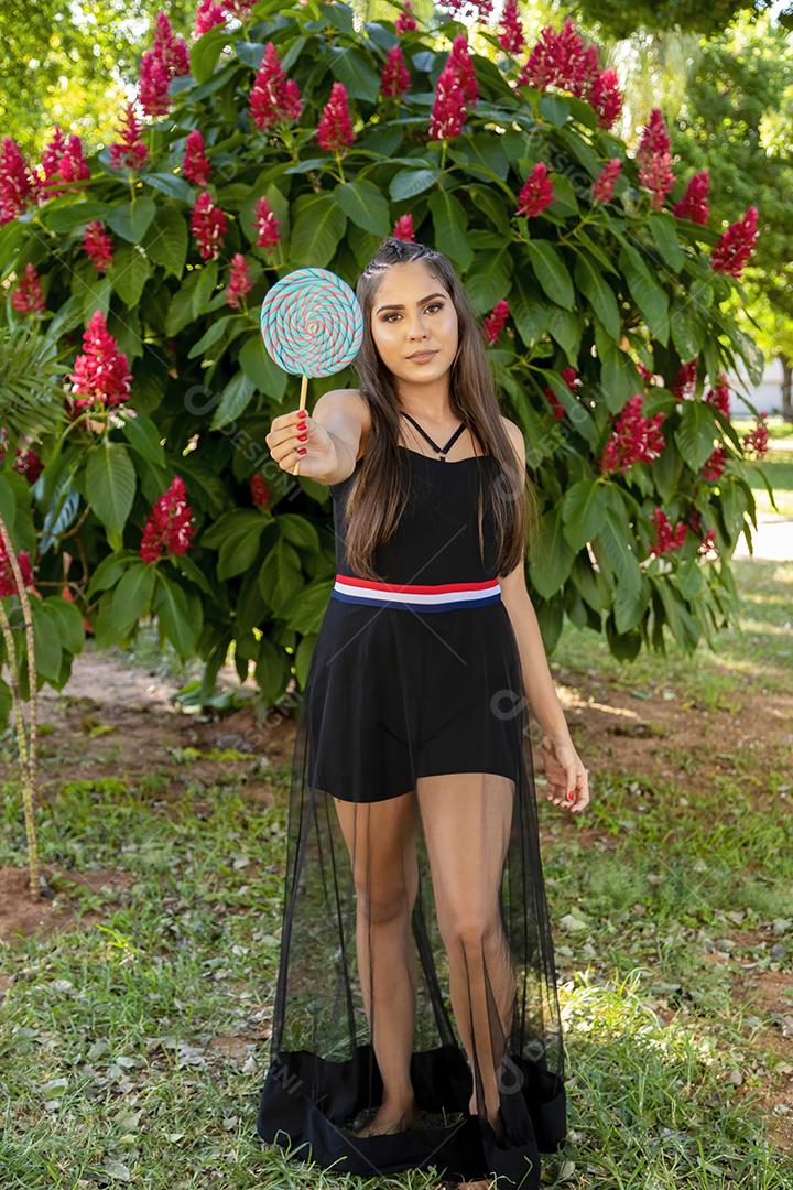 Linda menina morena segurando pirulito colorido na floresta