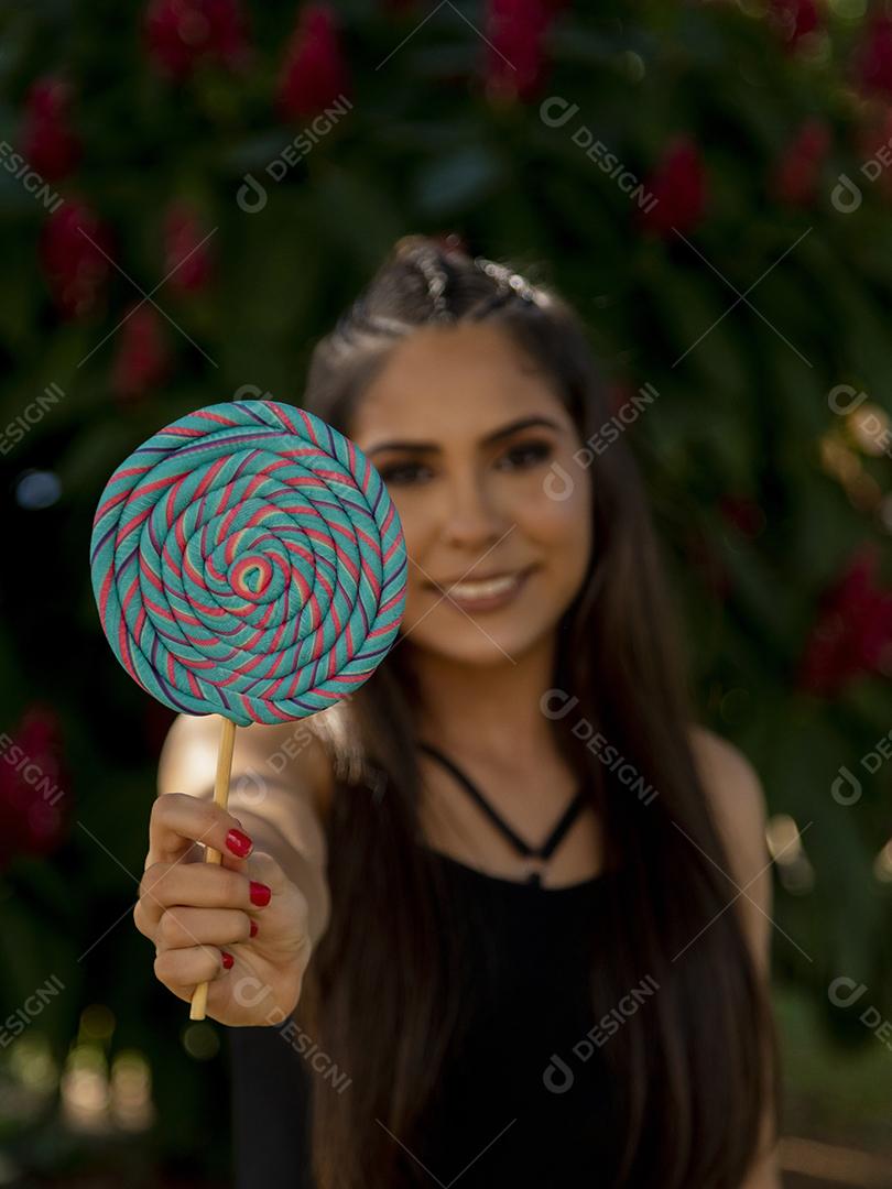 Linda menina morena segurando pirulito colorido na floresta