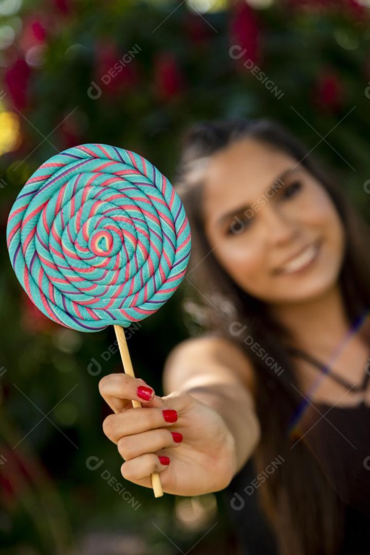 Linda menina morena segurando pirulito colorido na floresta