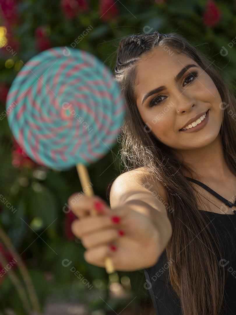 Linda menina morena segurando pirulito colorido na floresta
