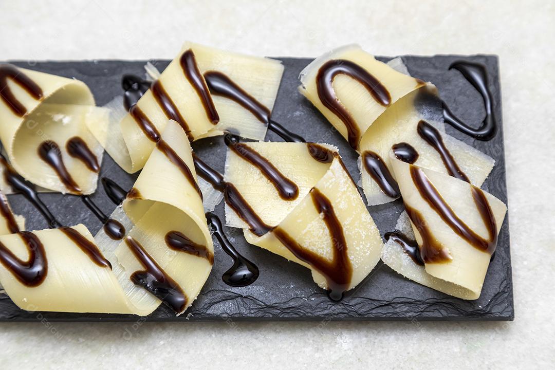 Porção de queijo parmesão em flocos com vinagre balsâmico em pedra preta