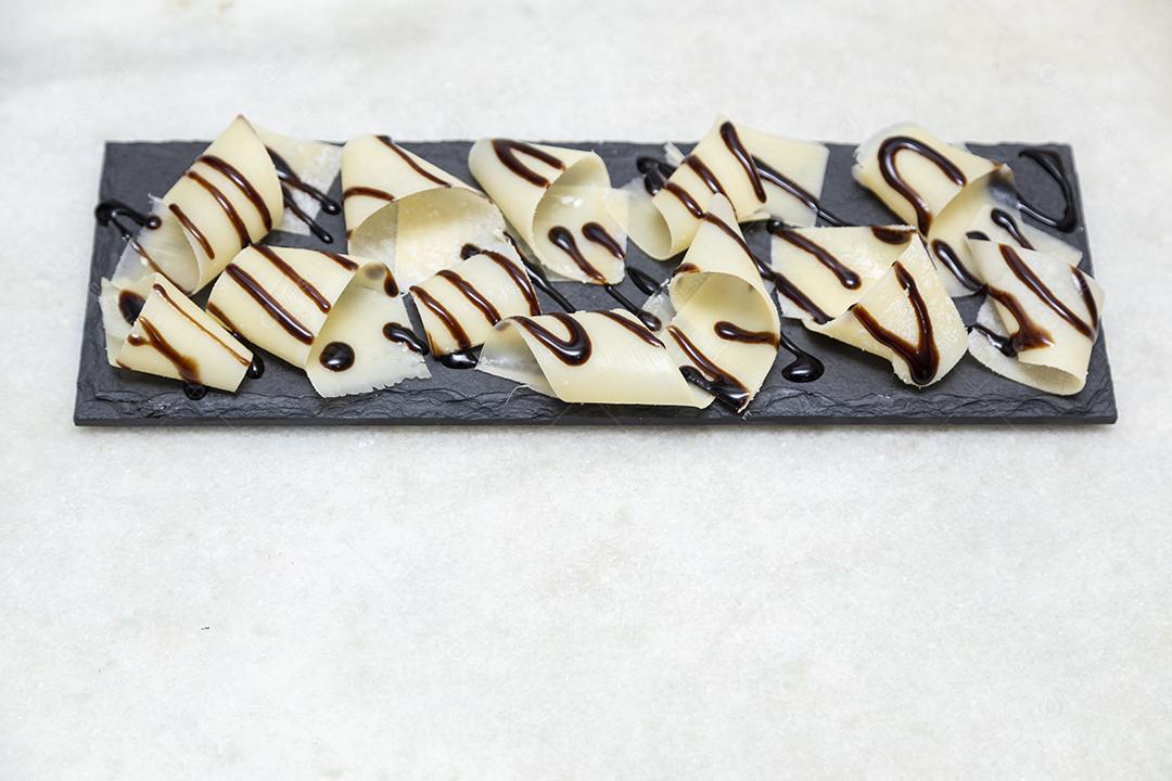 Porção de queijo parmesão em flocos com vinagre balsâmico em pedra preta