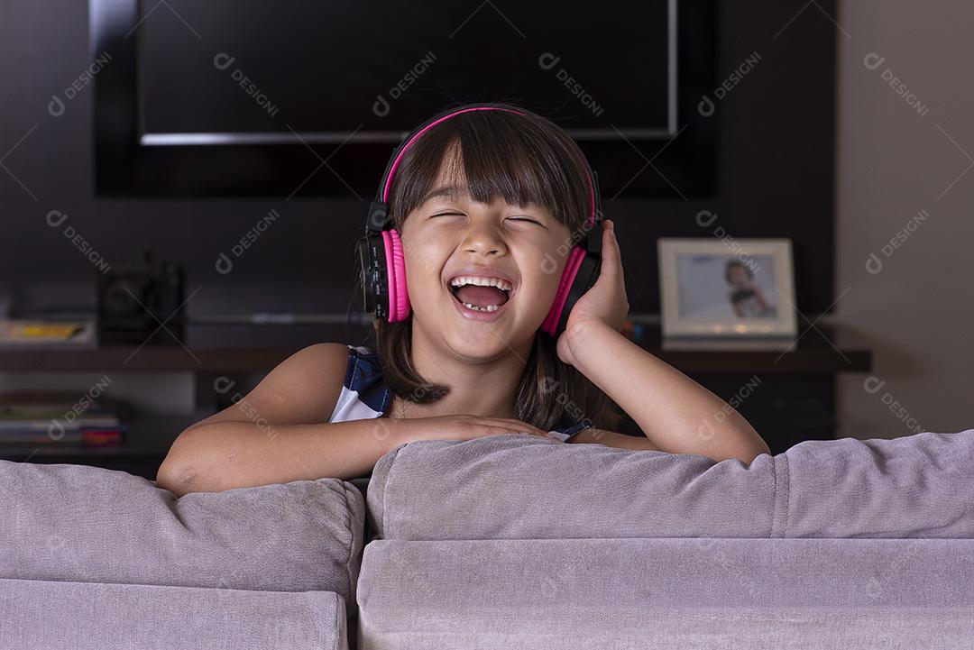 Menina bonitinha feliz ouvindo música no sofá em casa JPG