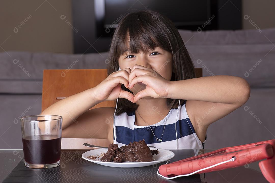 Menina bonita feliz assistindo tablet e comendo chocolate JPG