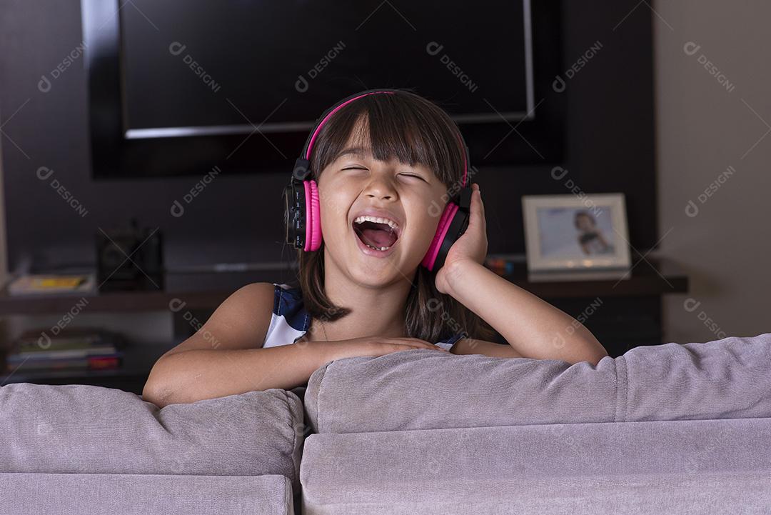 Menina bonitinha feliz ouvindo música no sofá em casa JPG