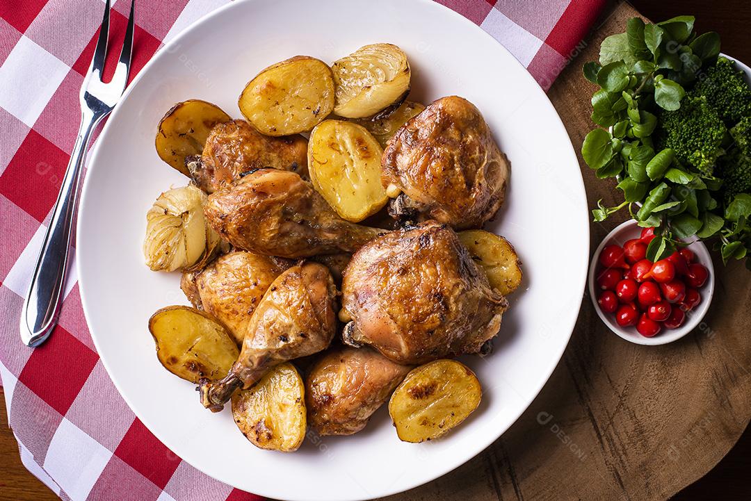 Frango assado em pedaços com batatas e cebola em um prato branco JPG