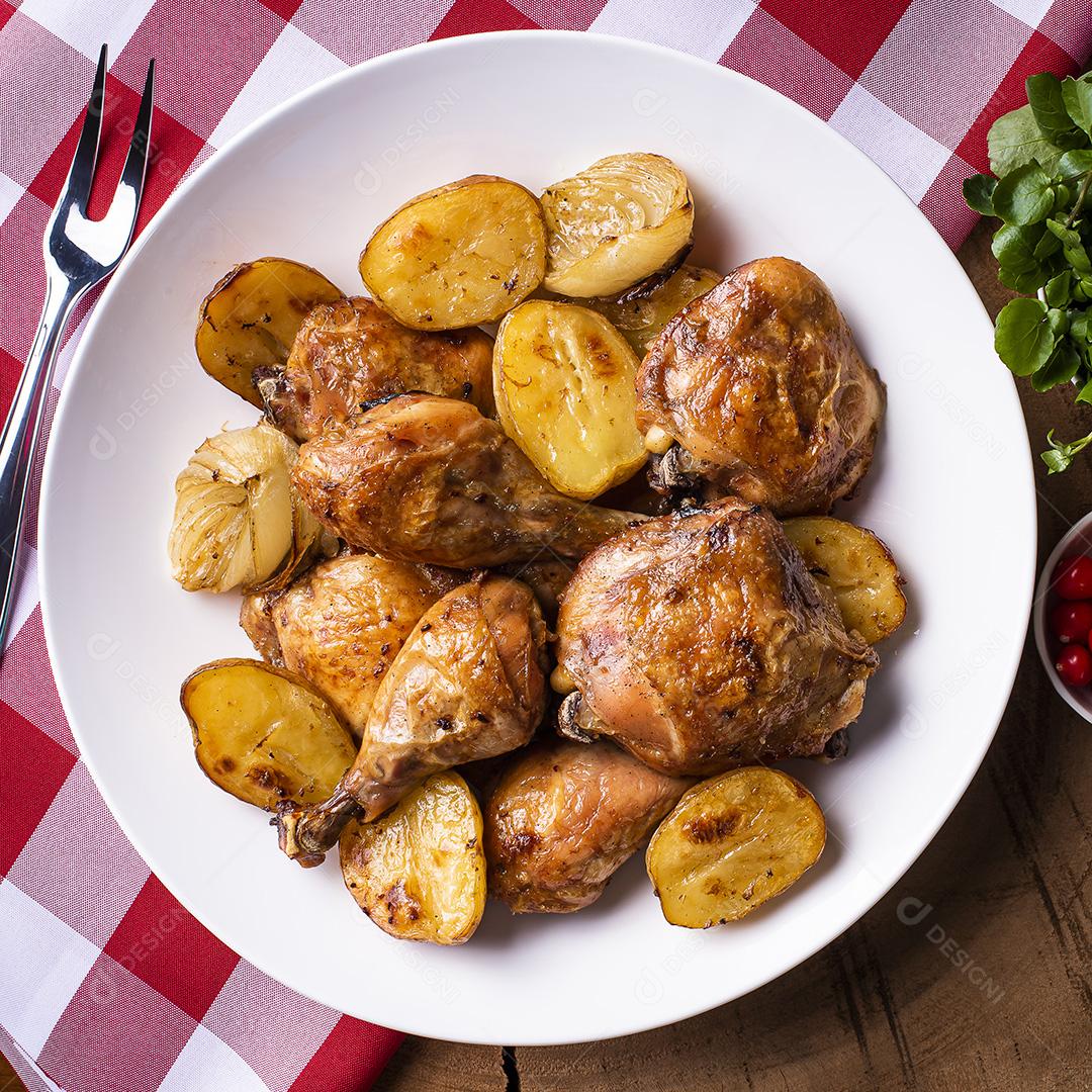 Frango assado em pedaços com batatas e cebola em um prato branco JPG