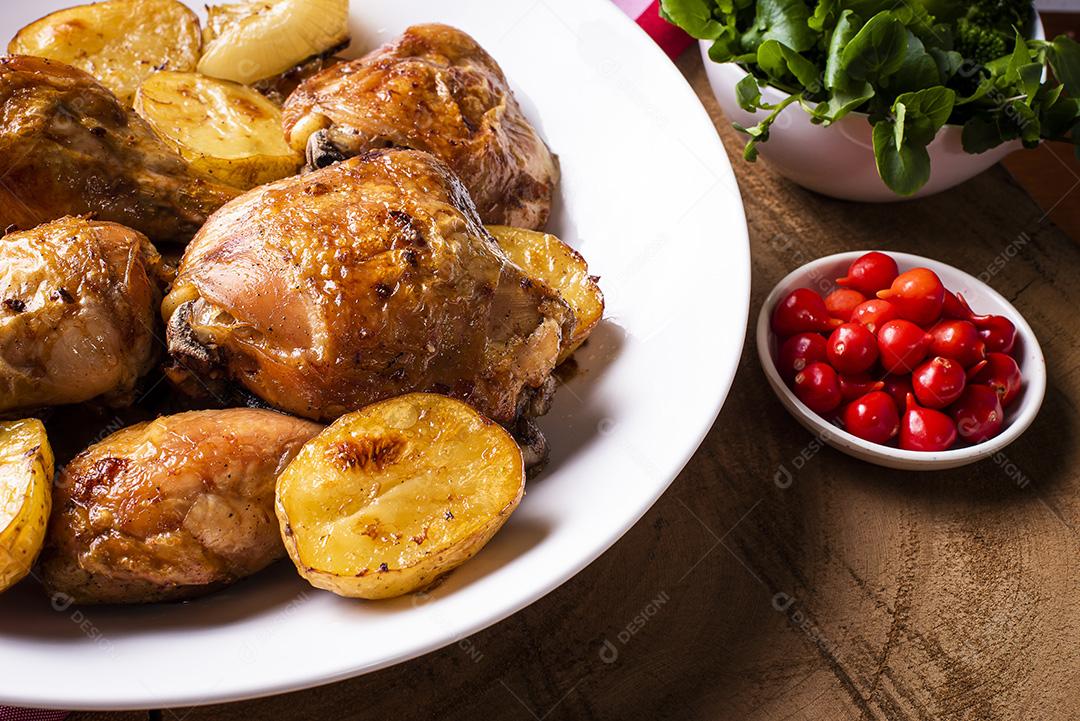 Frango assado em pedaços com batatas e cebola em um prato branco JPG