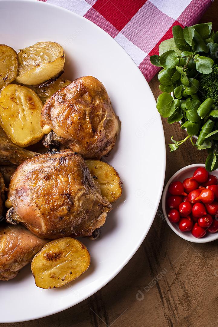 Frango assado em pedaços com batatas e cebola em um prato branco JPG