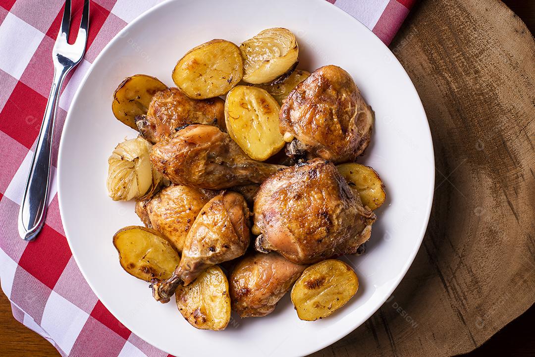 Frango assado em pedaços com batatas e cebola em um prato branco JPG