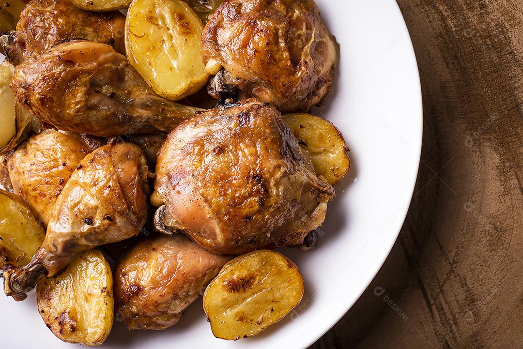 Frango assado em pedaços com batatas e cebola em um prato branco JPG