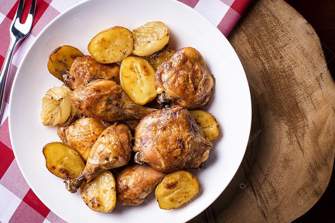 Frango assado em pedaços com batatas e cebola em um prato branco JPG