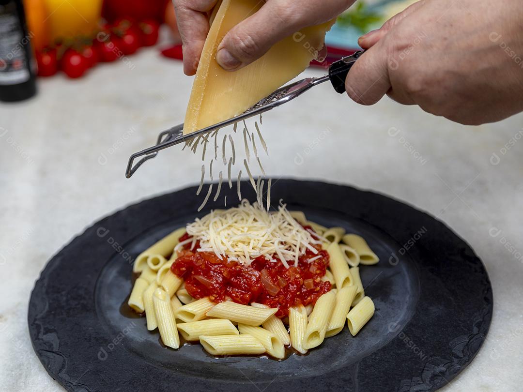 Massa penne com molho vermelho e queijo parmesão em um prato preto