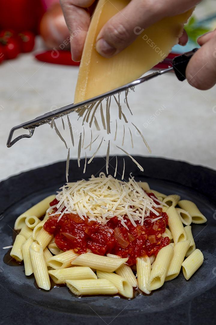 Massa penne com molho vermelho e queijo parmesão em um prato preto