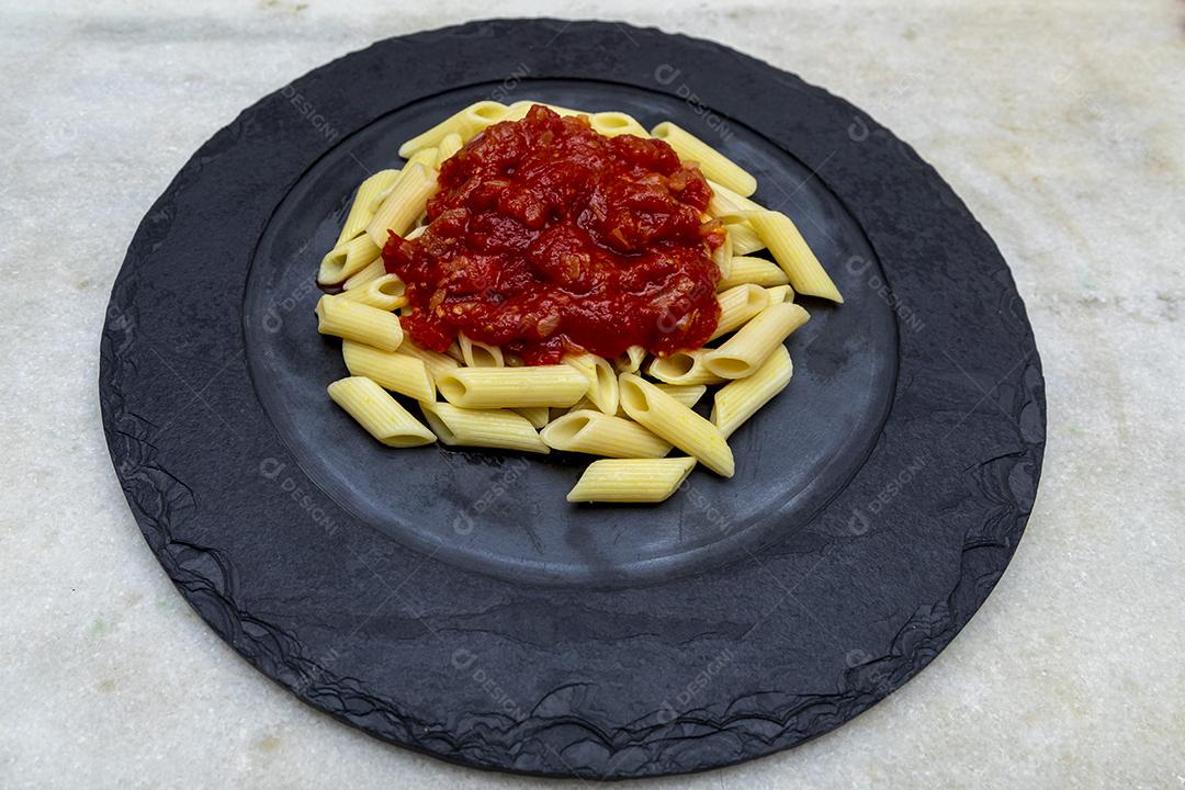 Massa penne com molho vermelho e queijo parmesão em um prato preto