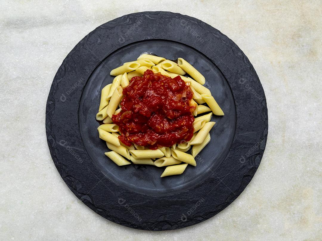 Massa penne com molho vermelho e queijo parmesão em um prato preto