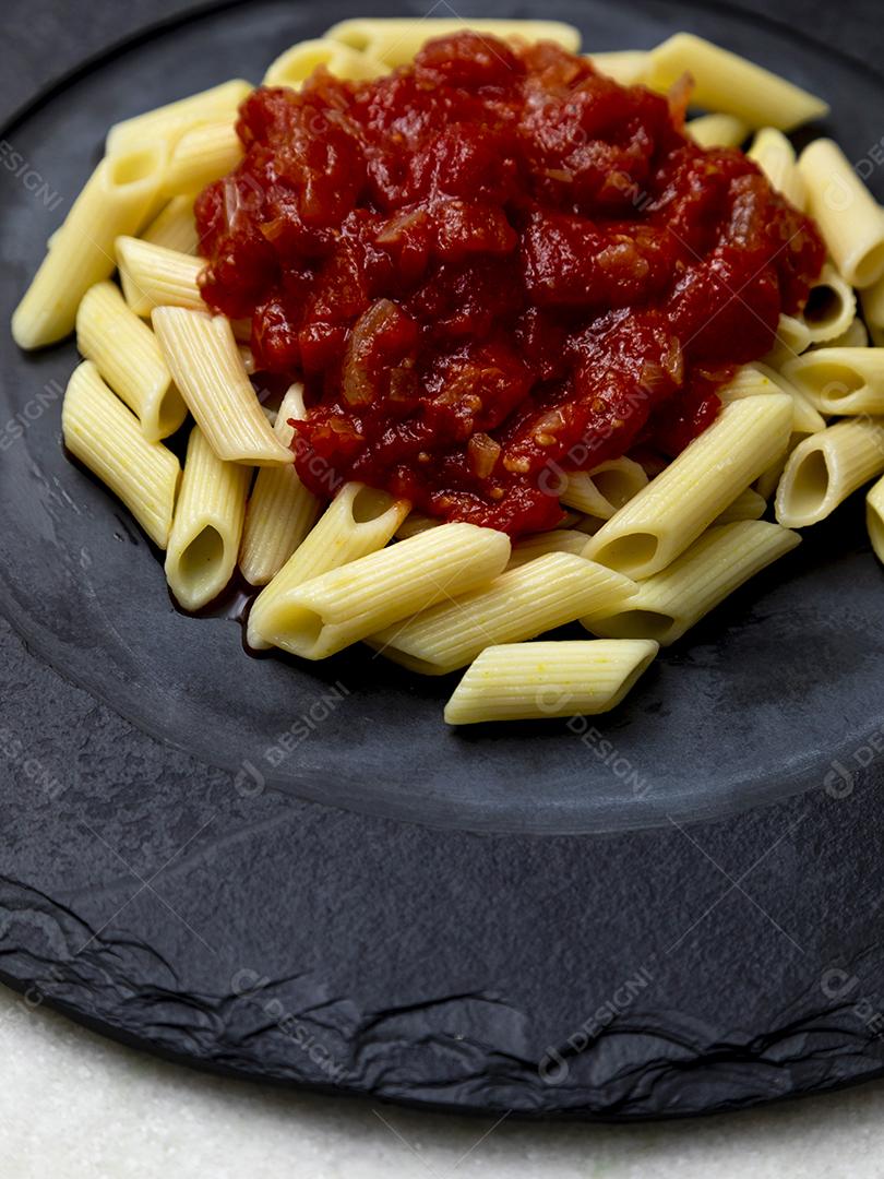 Massa penne com molho vermelho e queijo parmesão em um prato preto