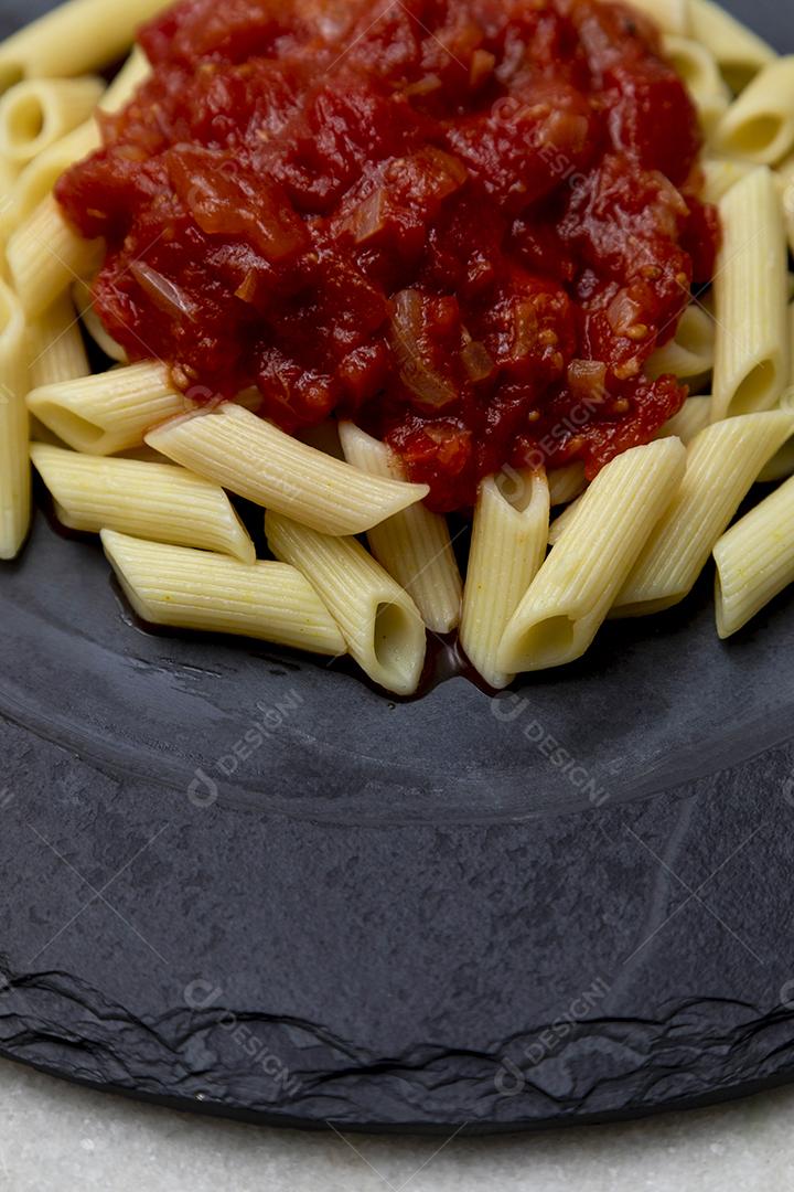Massa penne com molho vermelho e queijo parmesão em um prato preto