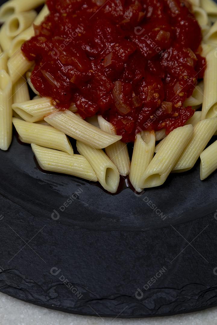 Massa penne com molho vermelho e queijo parmesão em um prato preto