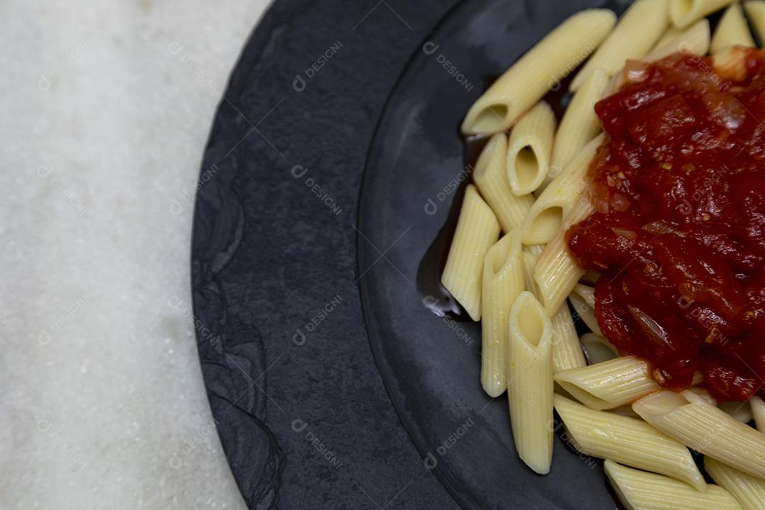 Massa penne com molho vermelho e queijo parmesão em um prato preto