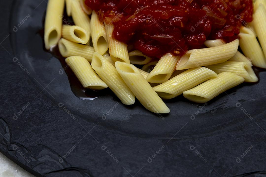 Massa penne com molho vermelho e queijo parmesão em um prato preto