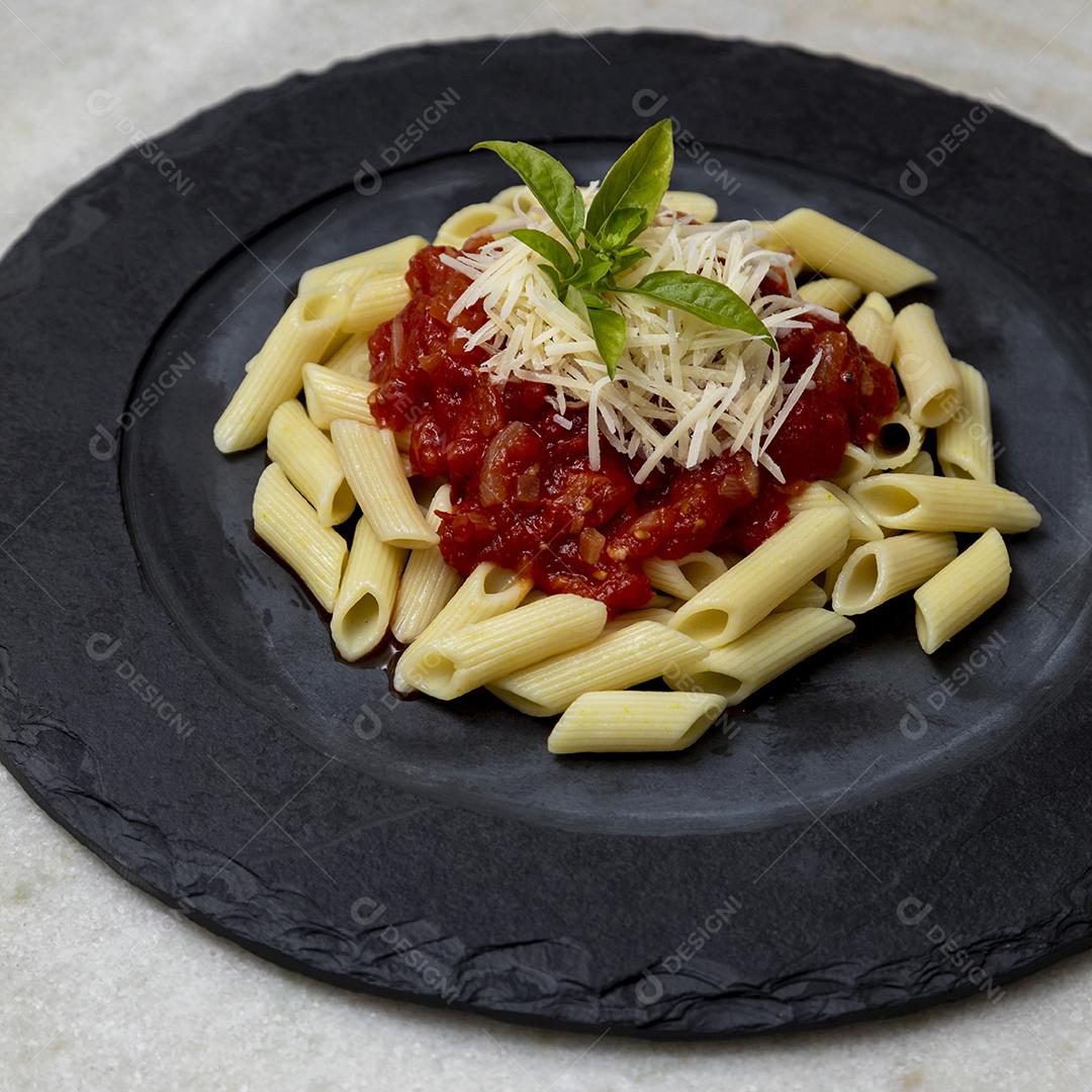 Massa penne com molho vermelho e queijo parmesão em um prato preto